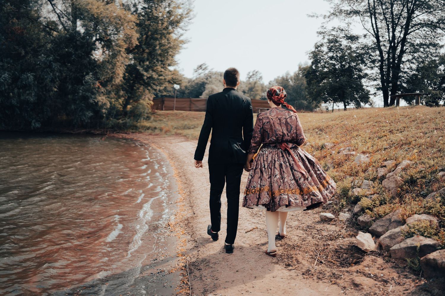 Couple in vintage clothing walking together along a winding riverside path on an autumn day.
