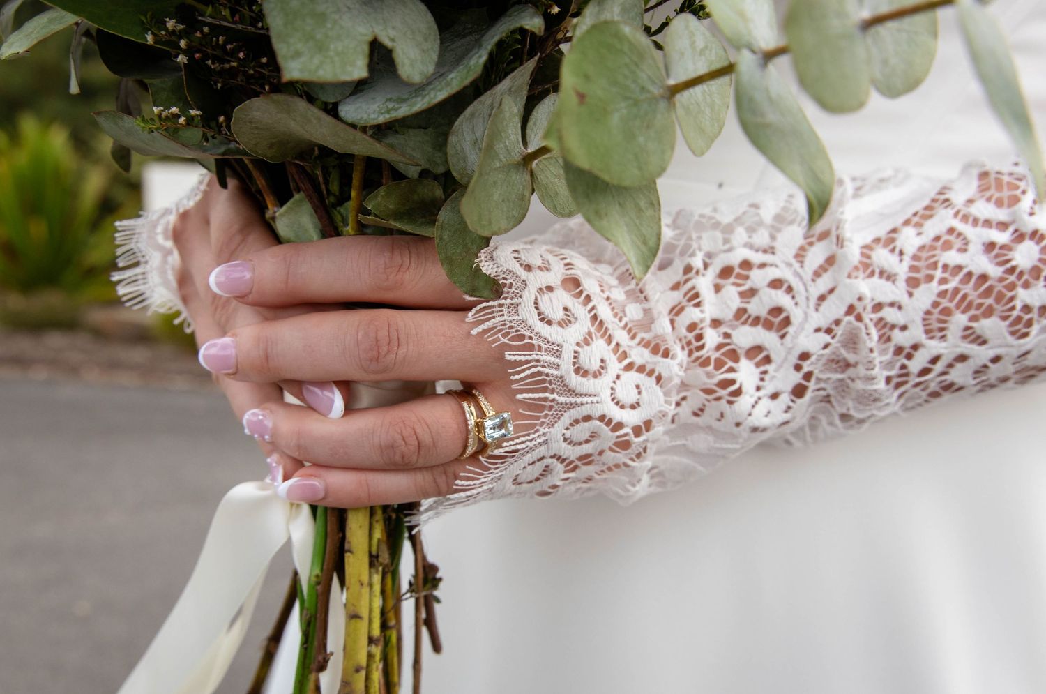 A close-up of delicate lace sleeve details and a bouquet being held with a ring adorned hand.