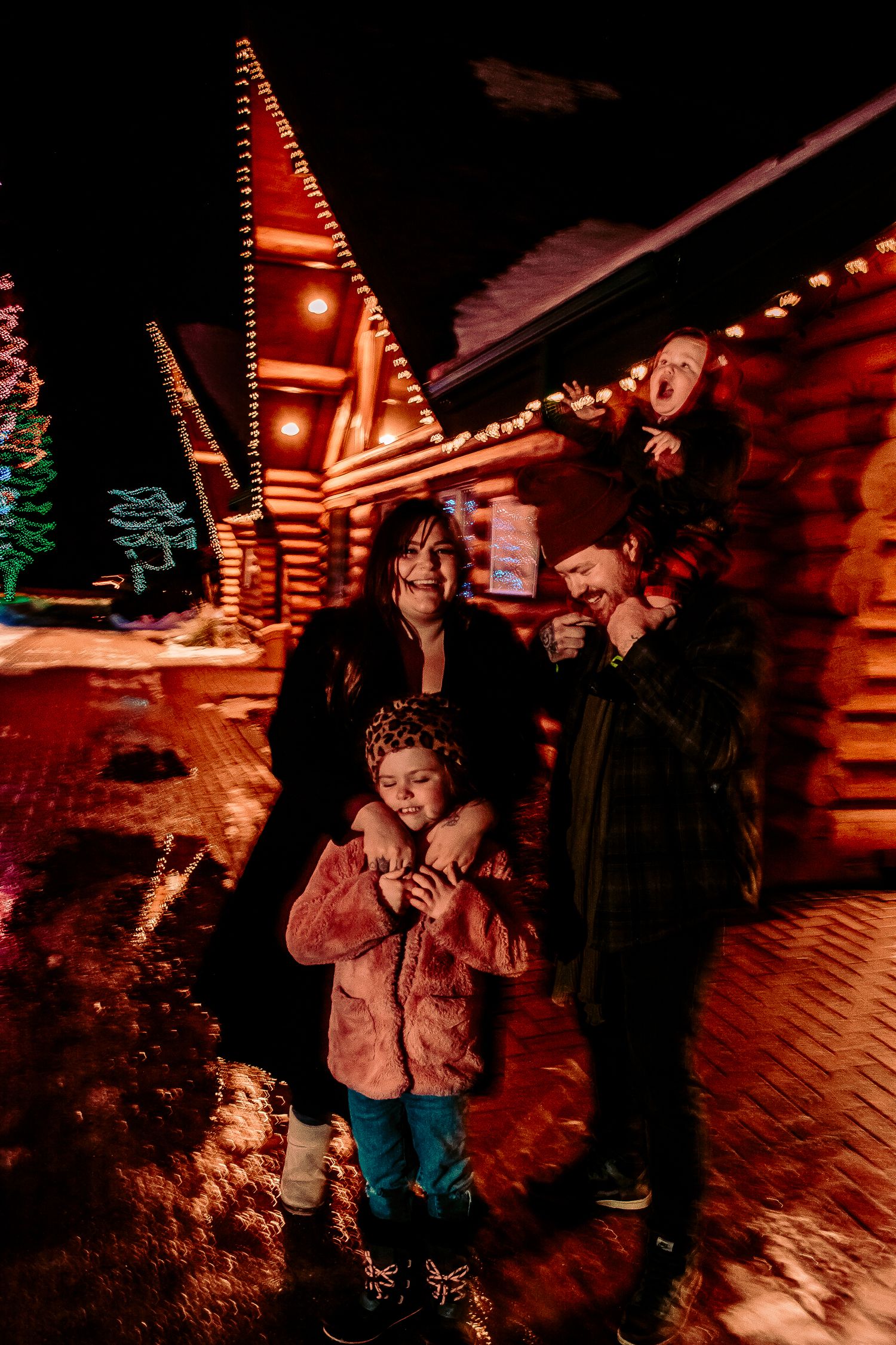 Family portrait at night with festive cabin lights and Christmas decorations.