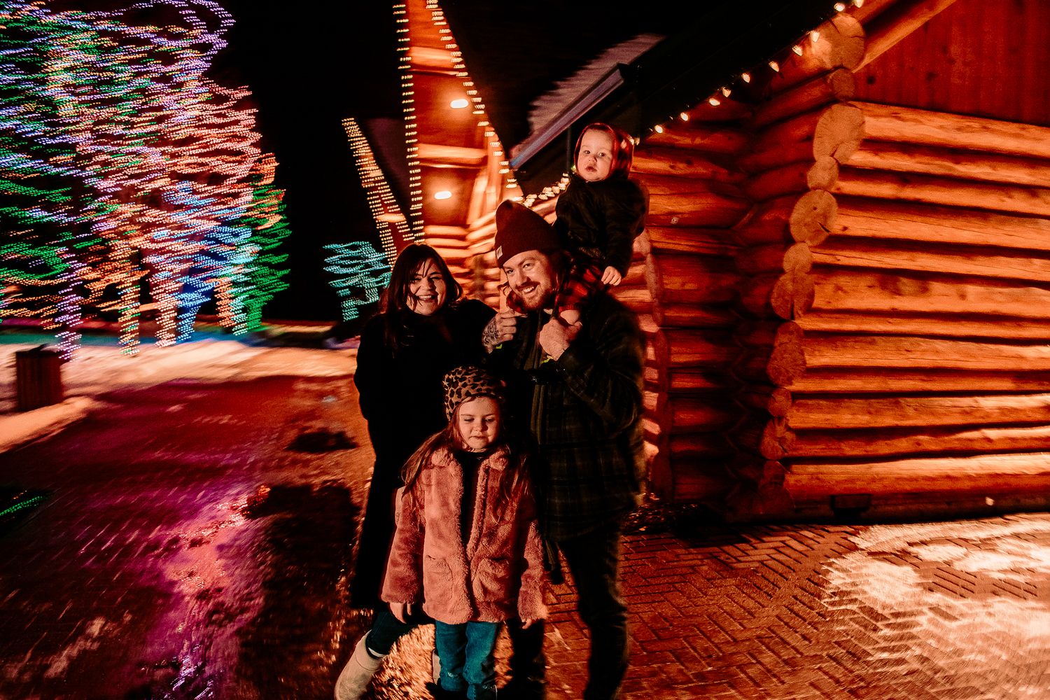 Family gathered outside rustic cabin with festive lights creating warm ambiance.