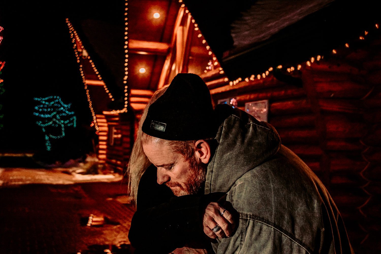 Intimate winter moment captured outside wooden cabins decorated with festive holiday lighting.