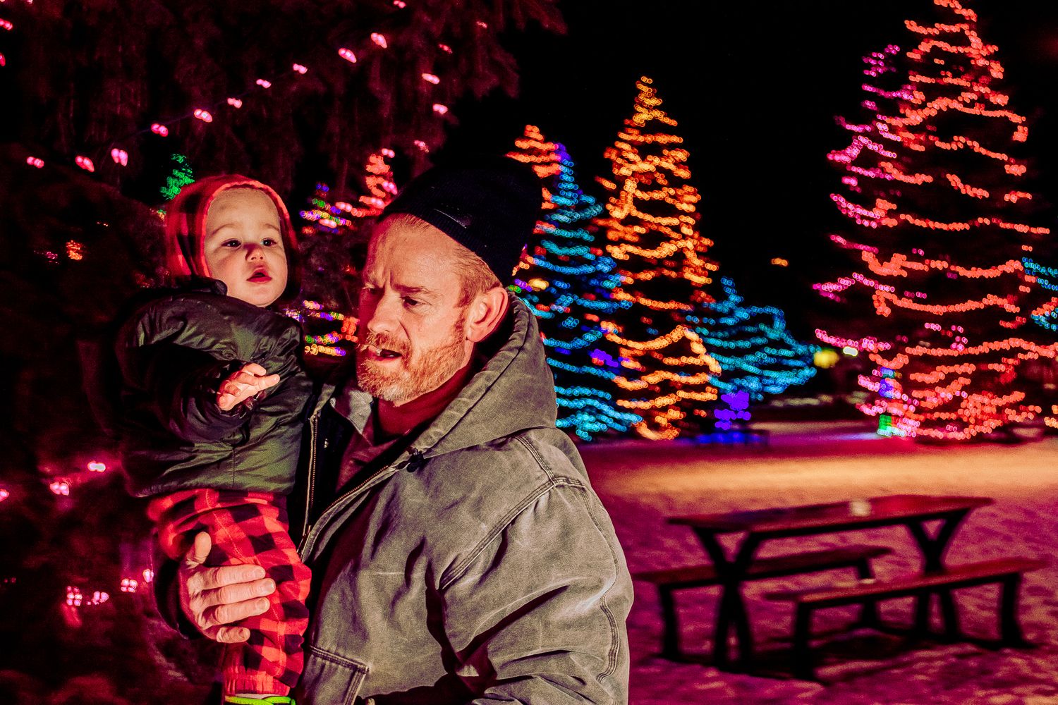 Winter evening portrait with illuminated Christmas trees glowing in blue and orange behind.