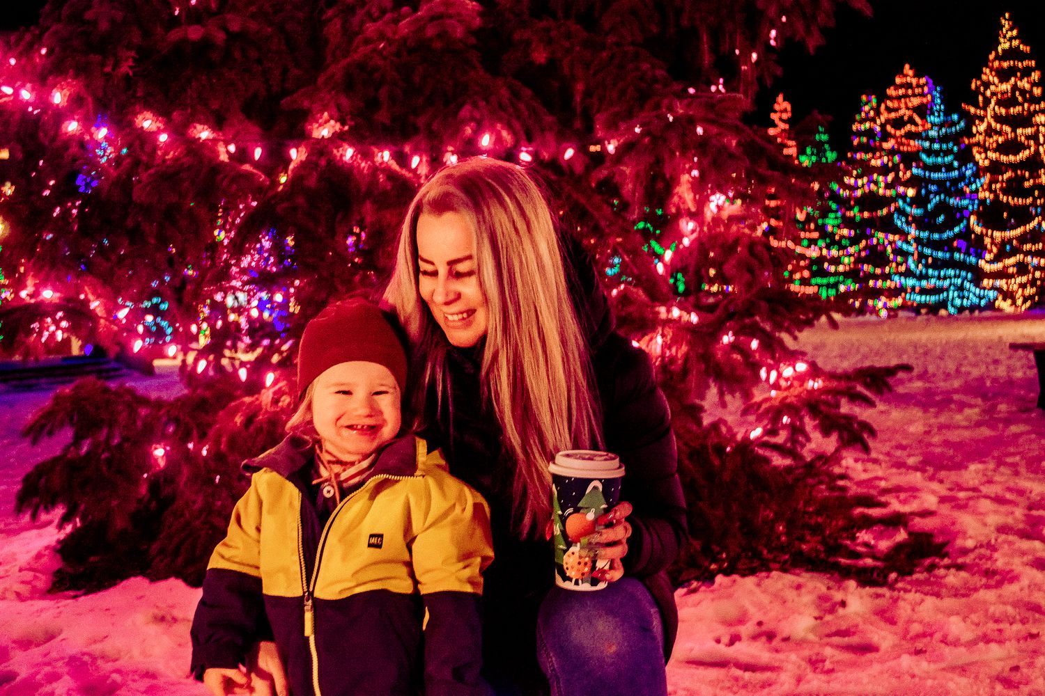 Festive winter scene with pink lights and colorful Christmas trees glowing in the background.