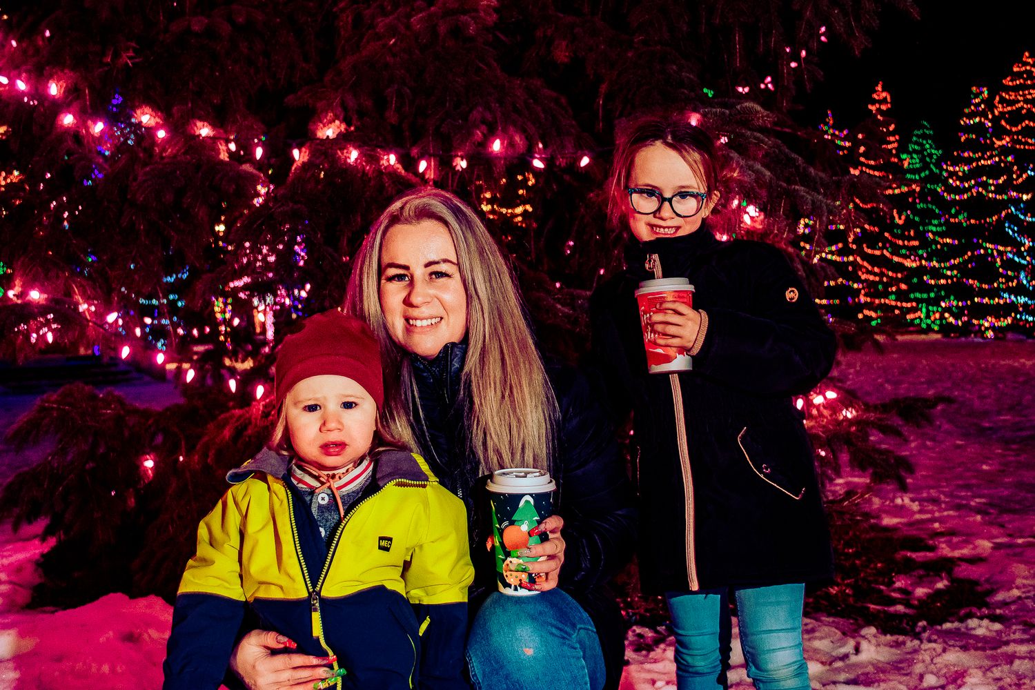 Winter portrait beneath pink holiday lights with illuminated Christmas trees in the background.