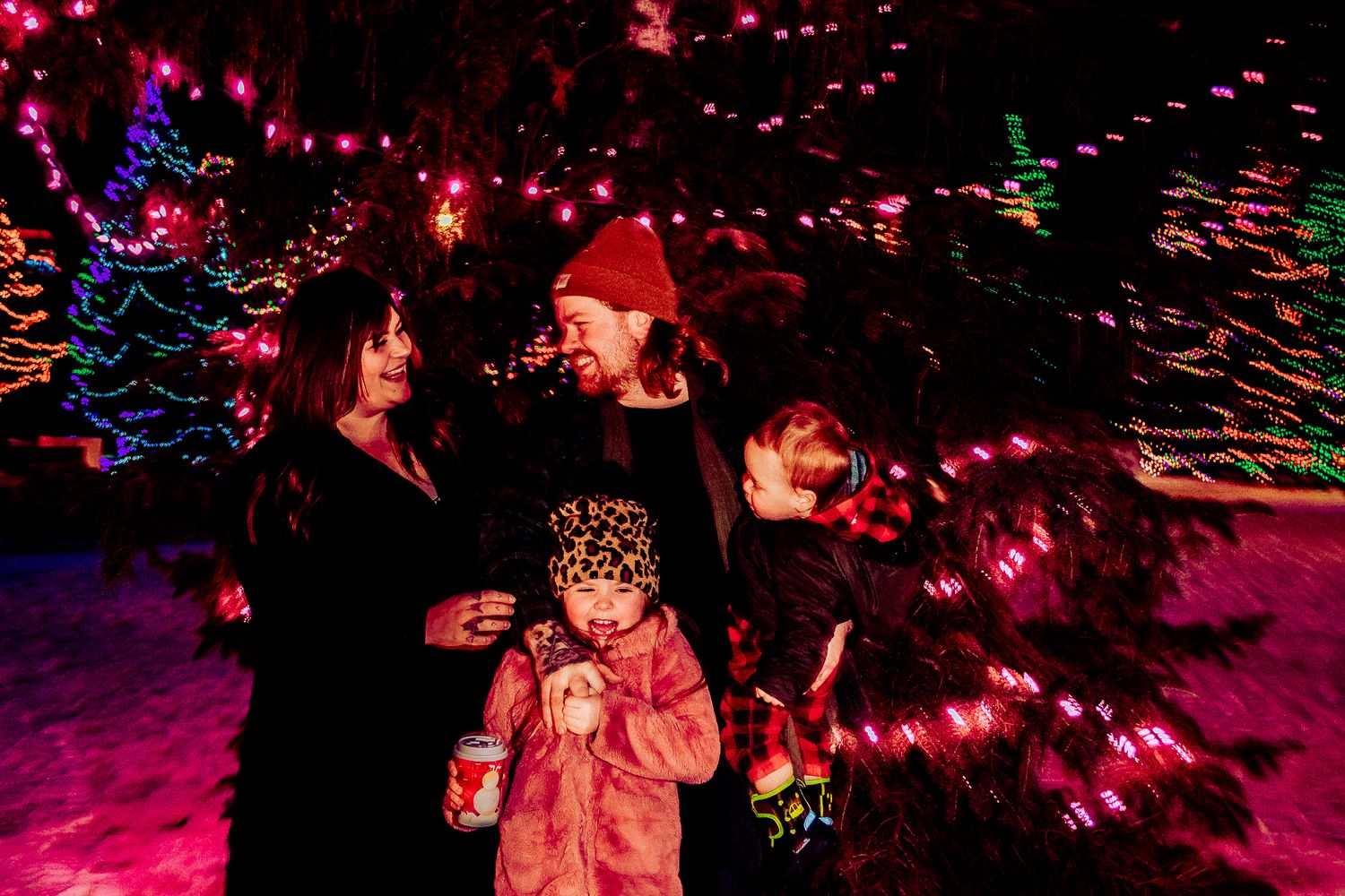 Family enjoying a winter evening under colorful Christmas lights in the snow.