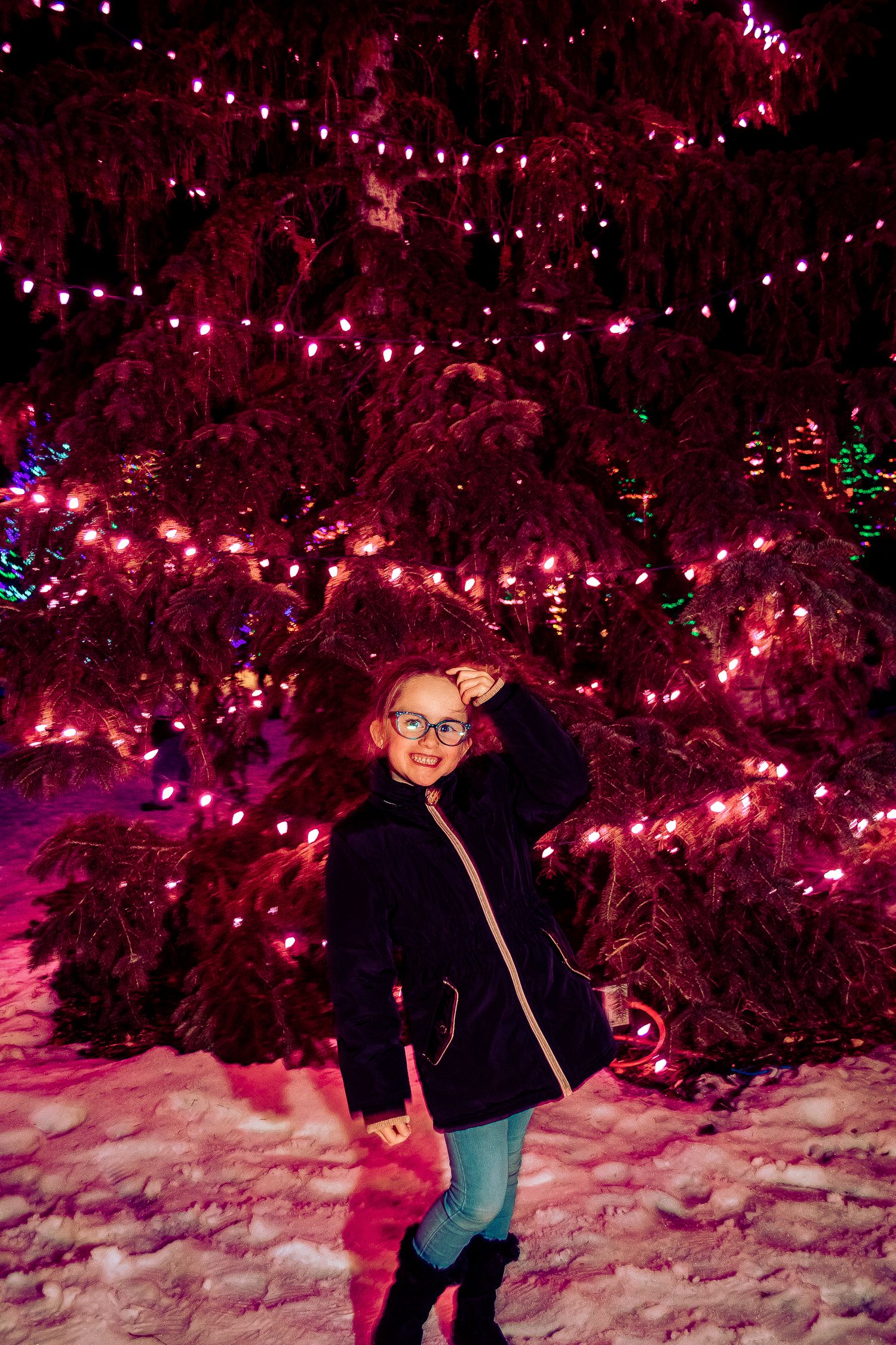 Nighttime winter scene with someone posing beneath trees decorated with pink holiday lights.