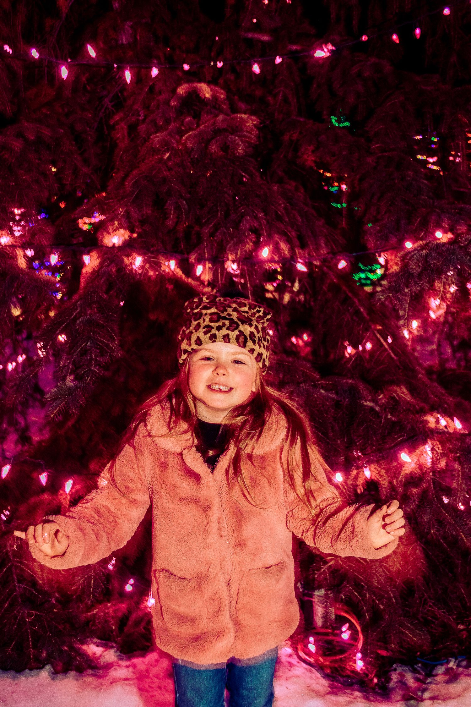 Winter portrait against a tree decorated with pink Christmas lights in the snow.