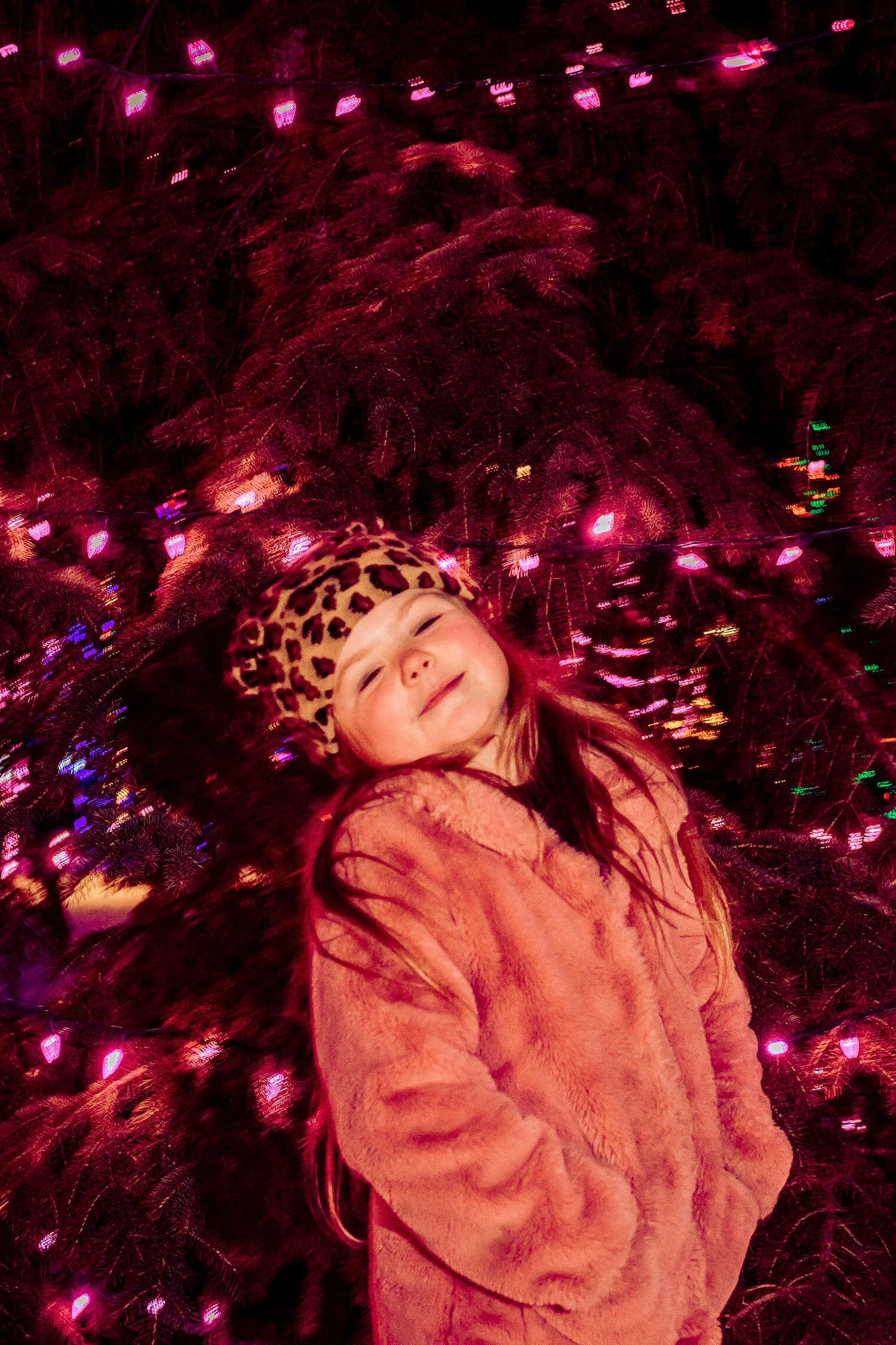 Artistic portrait beneath pink-lit holiday decorations wearing winter clothing.