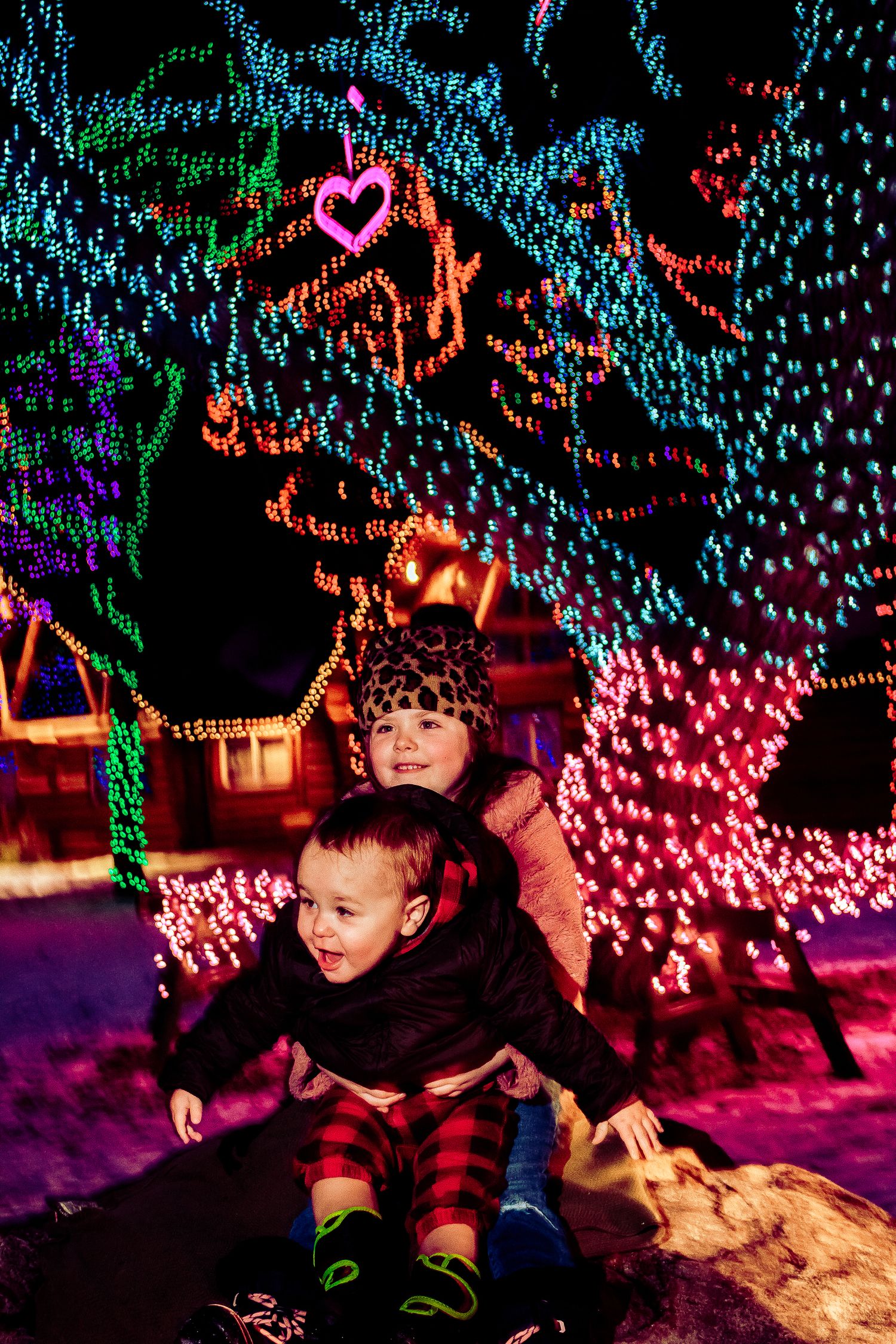 People sitting together on a rock surrounded by festive holiday lights and decorations in the snow.