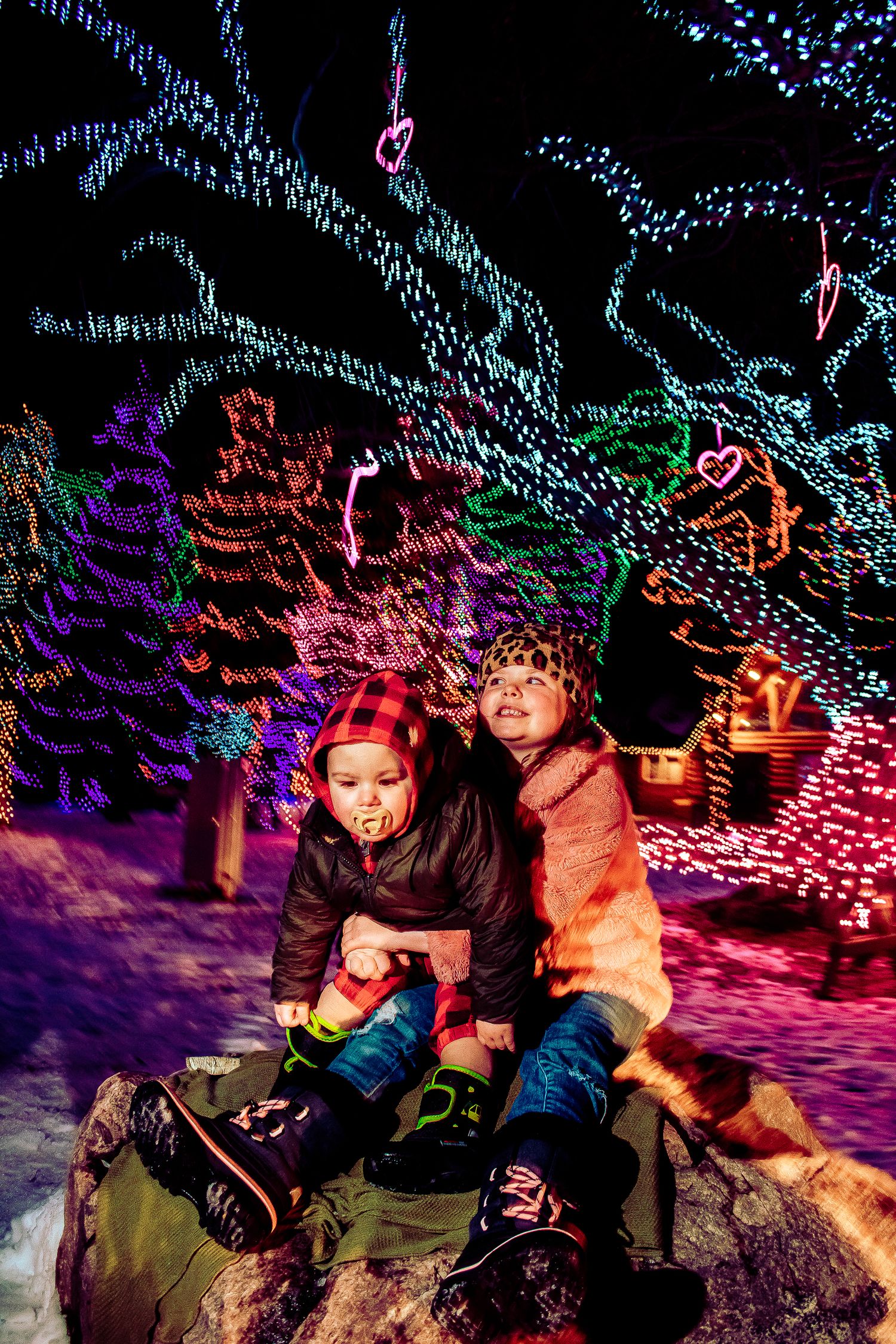 Two people sitting together on a rock surrounded by vibrant Christmas light displays.