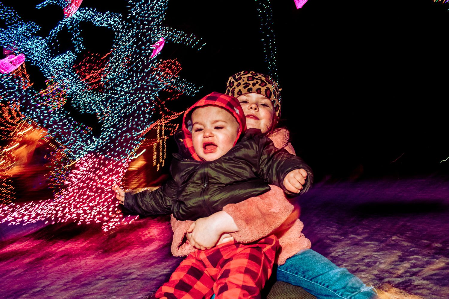 People playing and posing together on a rock with festive holiday lights behind them.