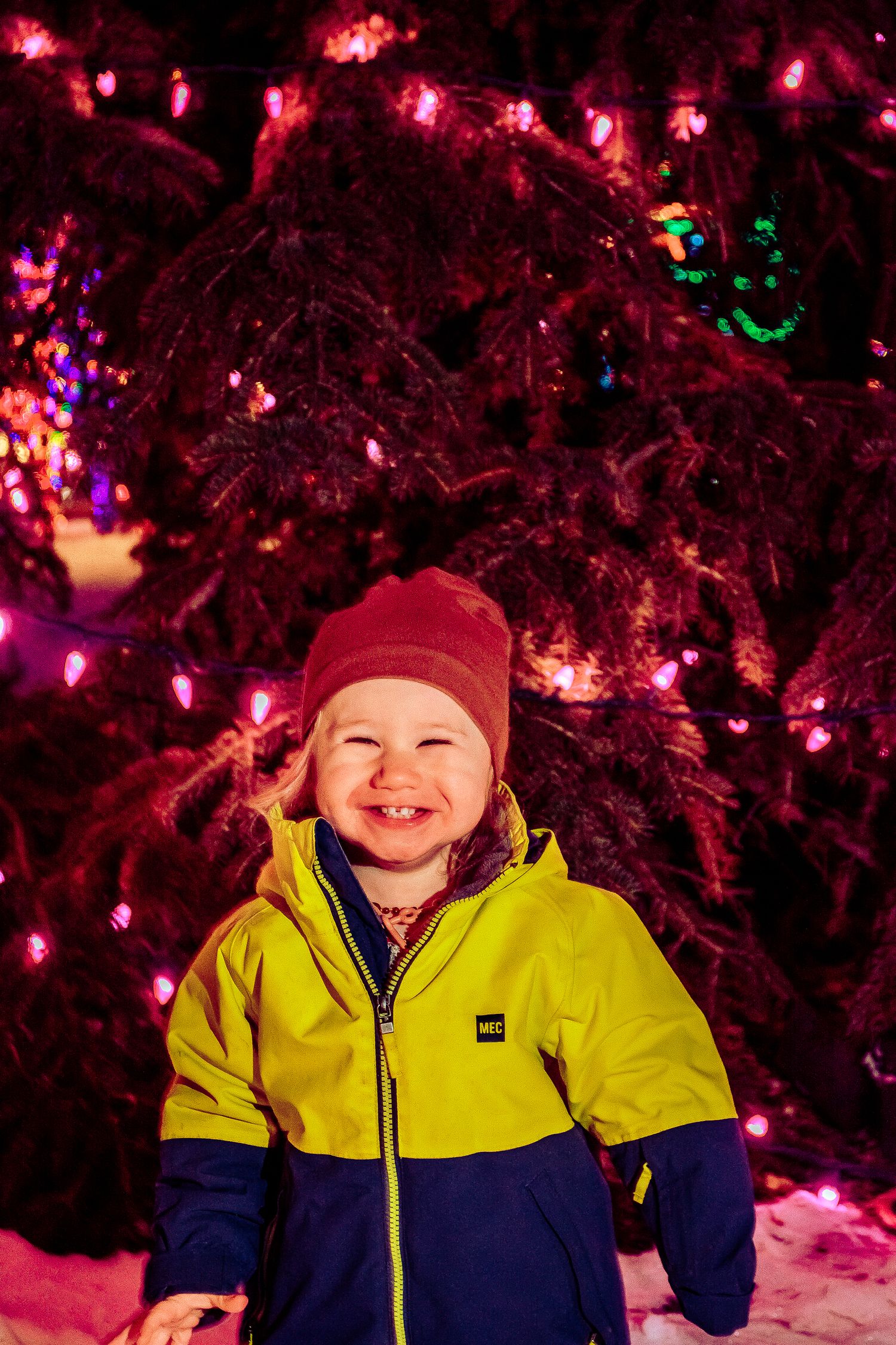 Winter portrait against glowing pink holiday lights wearing a bright yellow jacket.