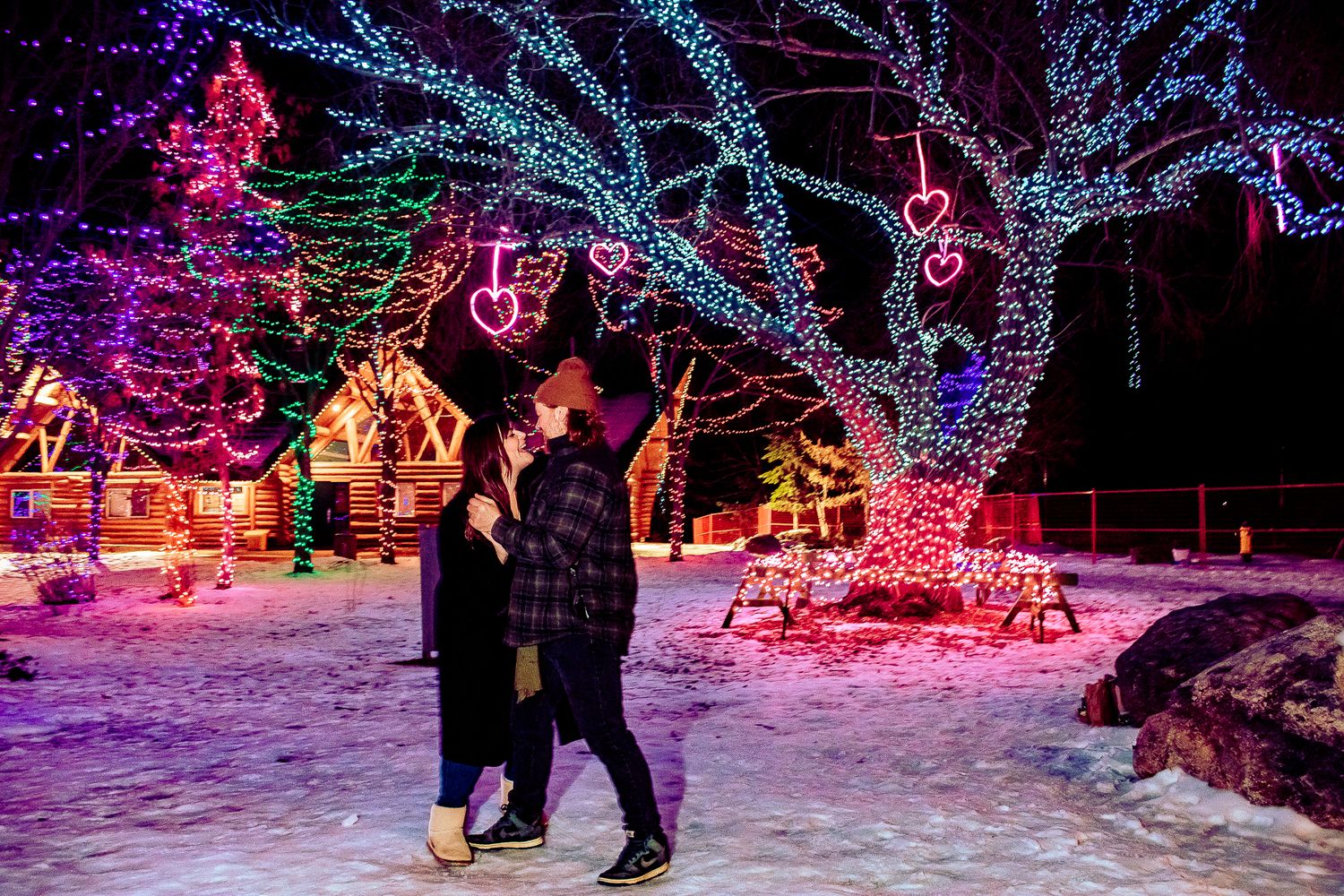 A couple walks through a winter wonderland of colorful Christmas lights and decorated houses.
