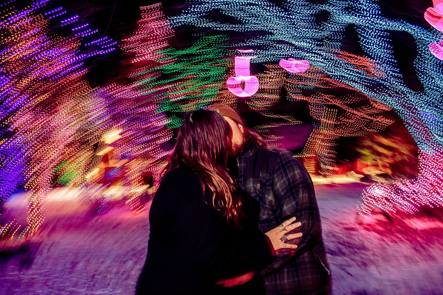 A couple sharing an intimate moment surrounded by vibrant holiday light decorations.