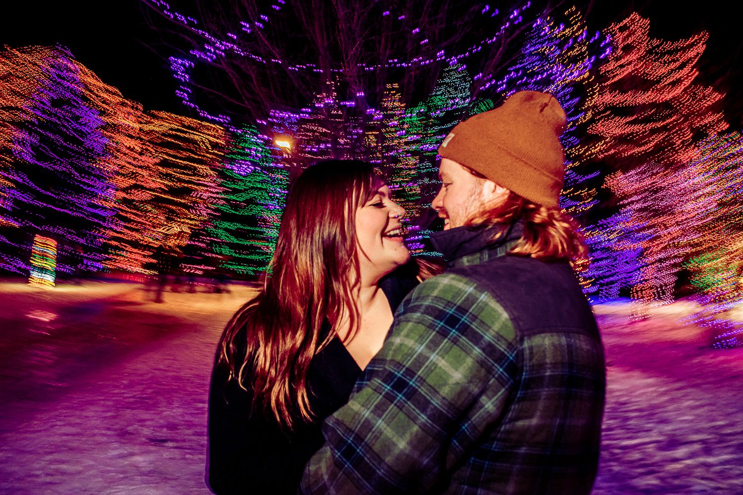 A romantic winter scene with holiday lights as a couple enjoys a tender moment in the snow.