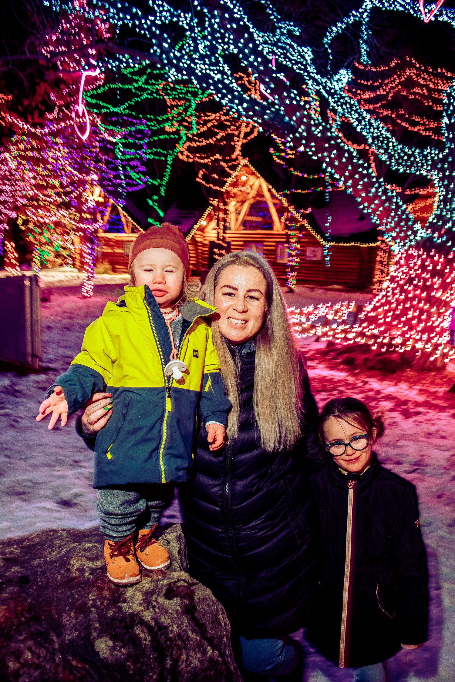 Group photo at a winter wonderland light display with colorful trees and illuminated decorations.