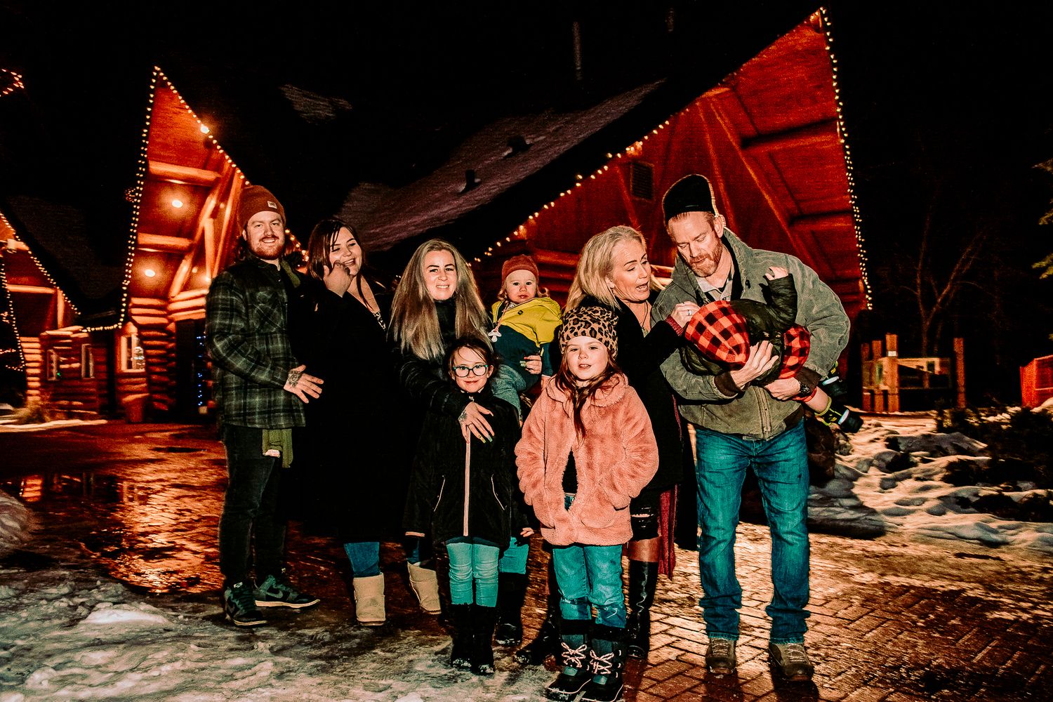 Group of people bundled up for winter standing in front of illuminated cabin structures.