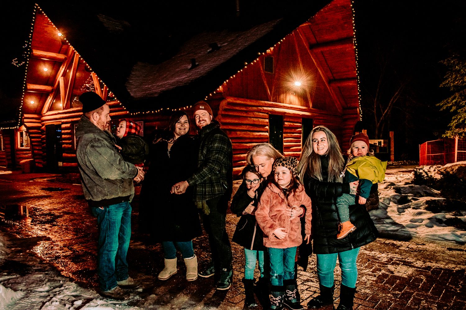 Family portrait in front of warmly lit wooden structures during winter evening.