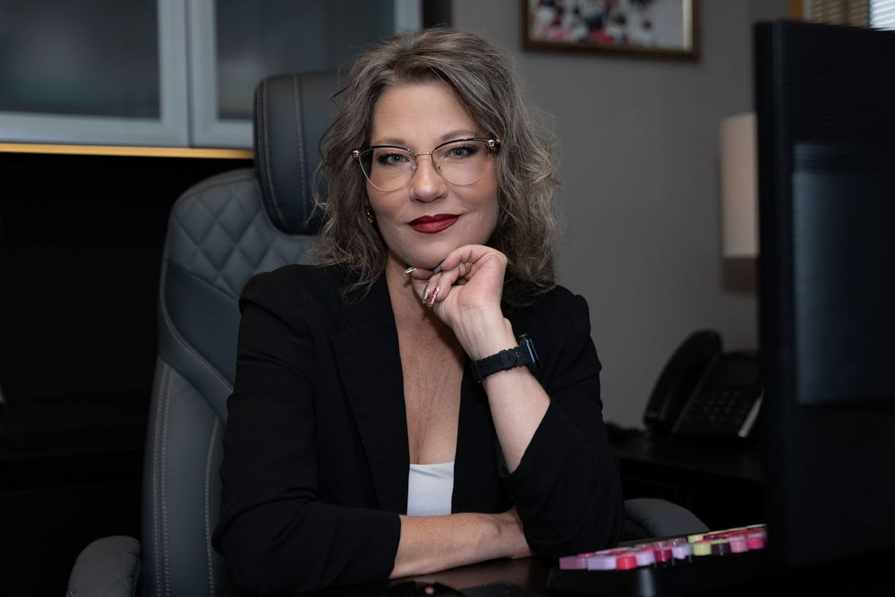 Professional office portrait showing a seated businesswoman in a black blazer at her desk.