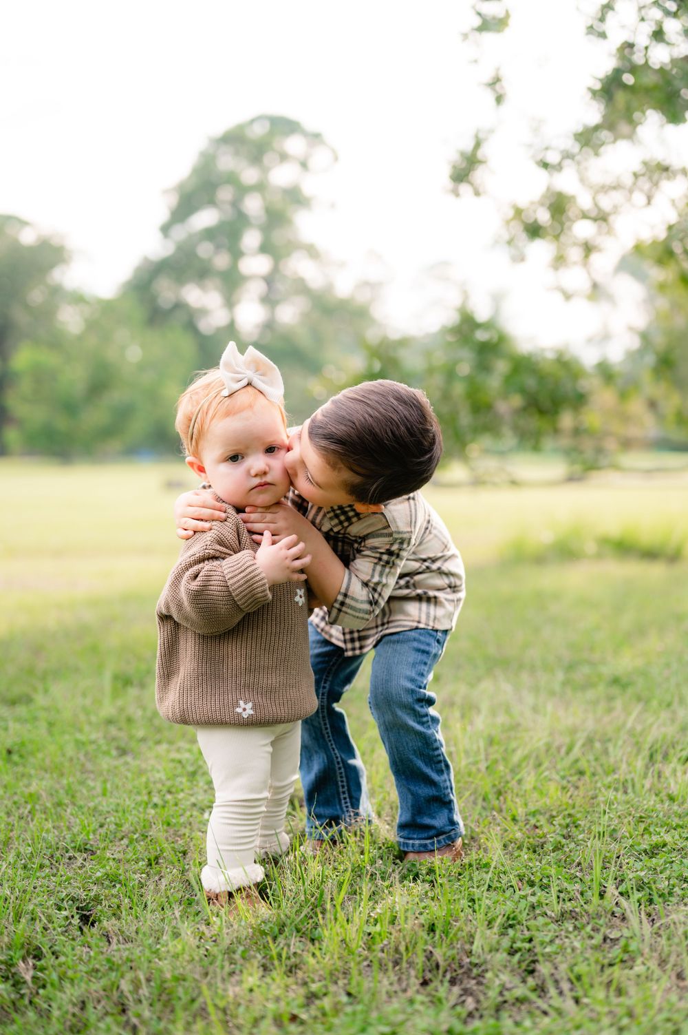 Two young children sharing a sweet moment while playing together in a grassy field on a sunny day.