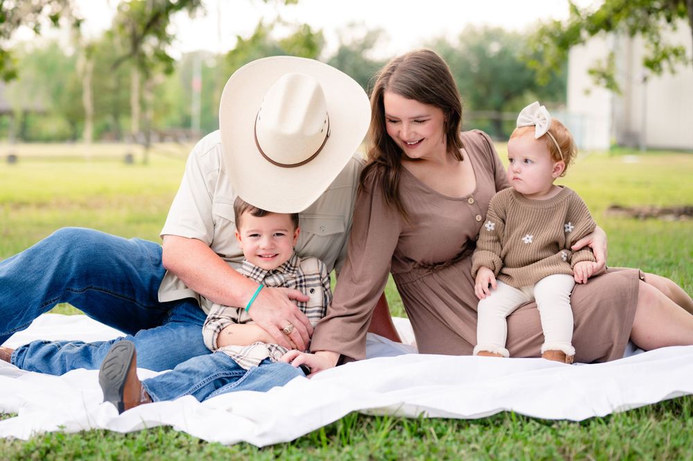 A family relaxes together on a white blanket during an outdoor photoshoot in casual attire.