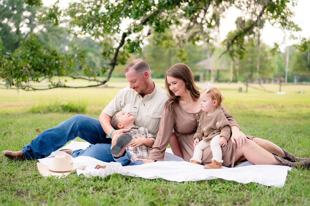 A family gathering on a white blanket for a casual outdoor photoshoot in neutral tones.