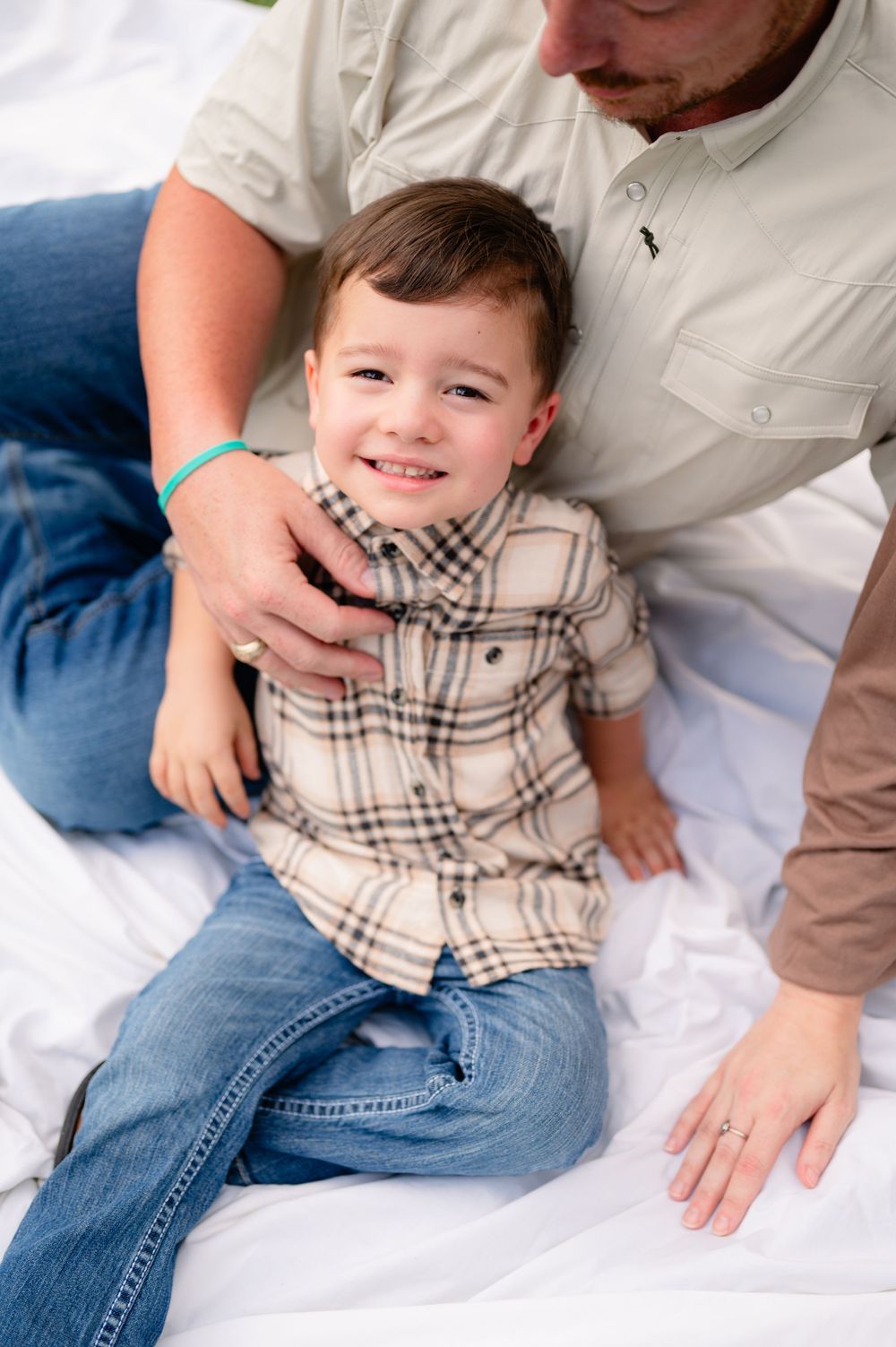 A candid moment of affection captured on a white blanket during an outdoor family photoshoot.