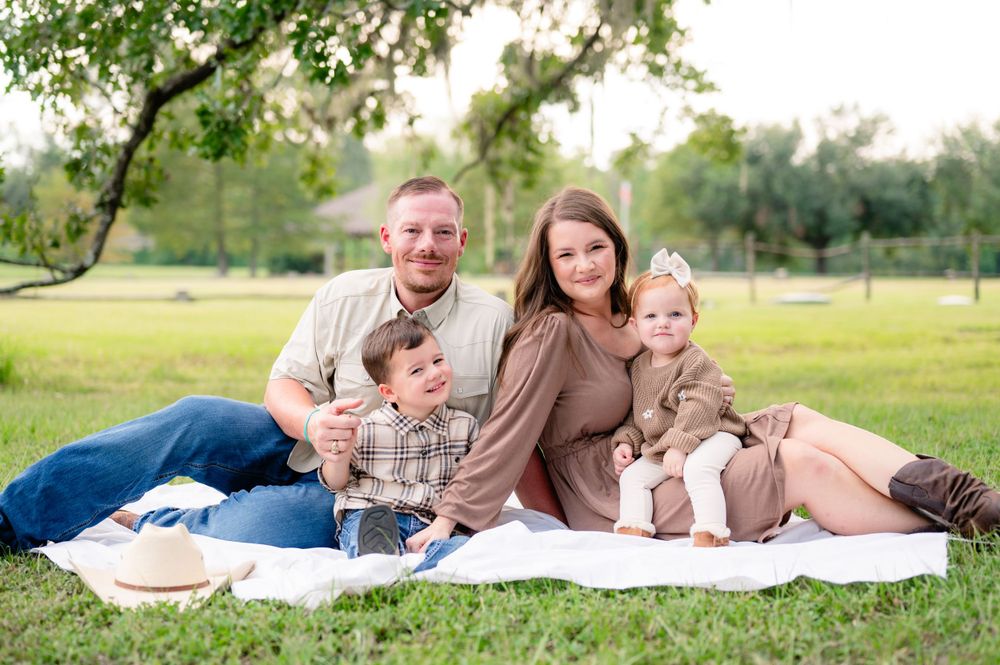 A relaxed family portrait session on a white blanket in a grassy field with natural lighting.