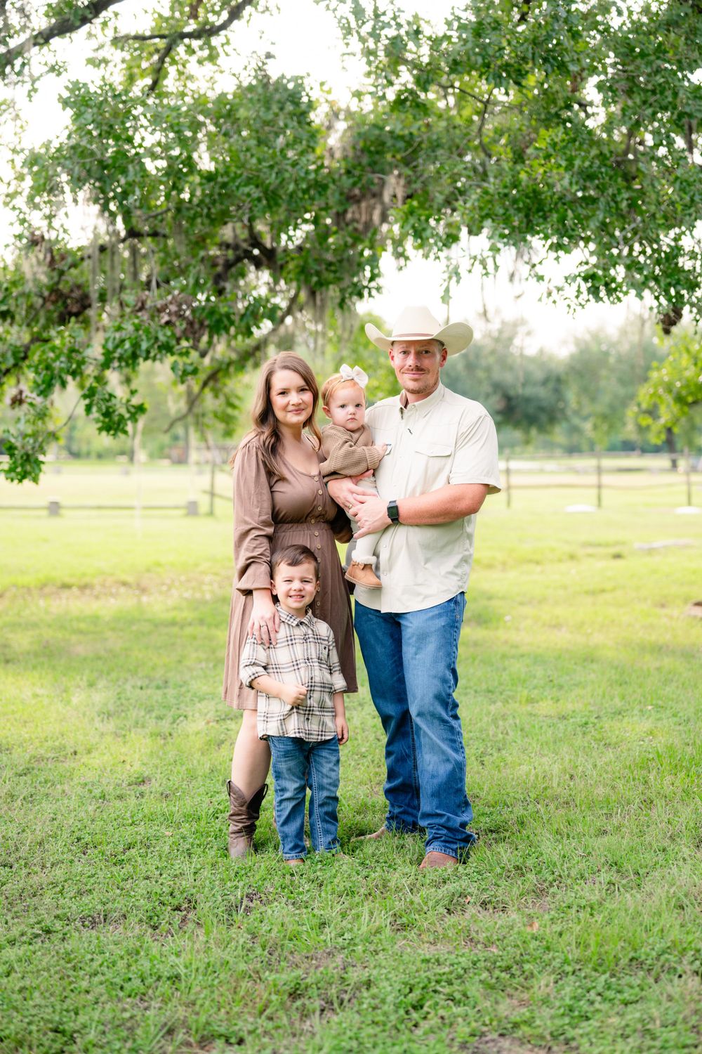 A country-style family portrait in a pastoral setting with a rustic wooden fence in the background.