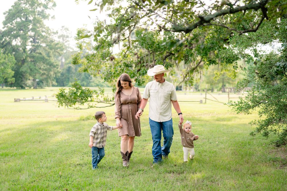 A family walking together through a sun-dappled field under green tree canopy.