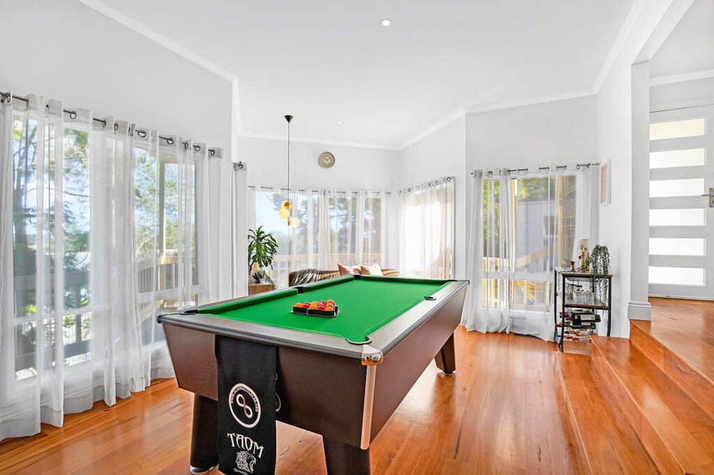 Bright game room with pool table, hardwood floors and white curtains covering large windows.