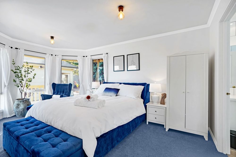 Luxurious bedroom with royal blue accents, white bedding, and sheer curtains framing windows.