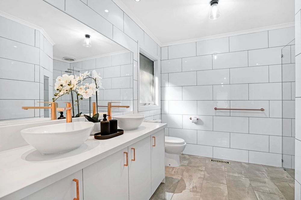 Modern white bathroom featuring vessel sinks, orchid decoration, and large subway tile walls.