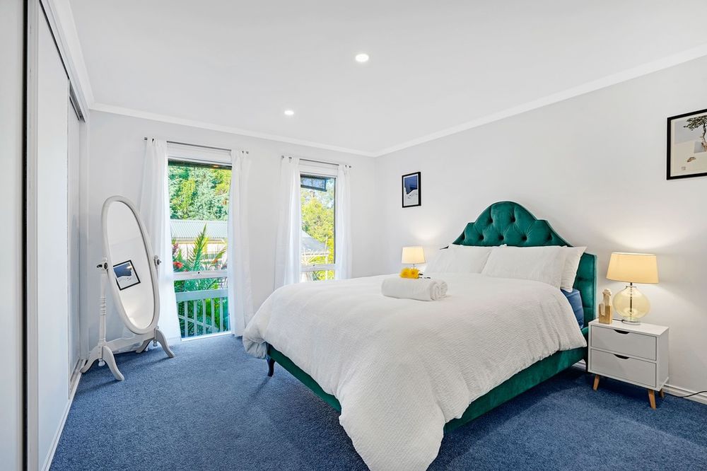 Bright bedroom with teal upholstered headboard, white bedding, and blue carpet floors.