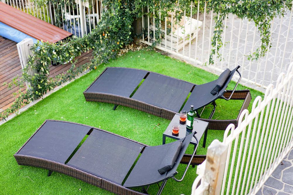 Two modern loungers on artificial grass in a fenced backyard patio area.