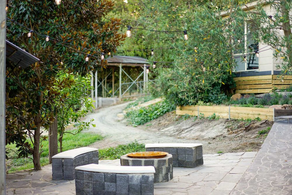 Outdoor garden path leading to stone fire pit seating area surrounded by lush greenery.