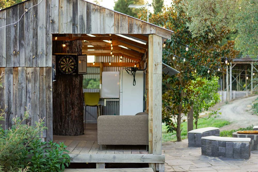 Rustic wooden shed with open doorway and deck patio surrounded by garden greenery.