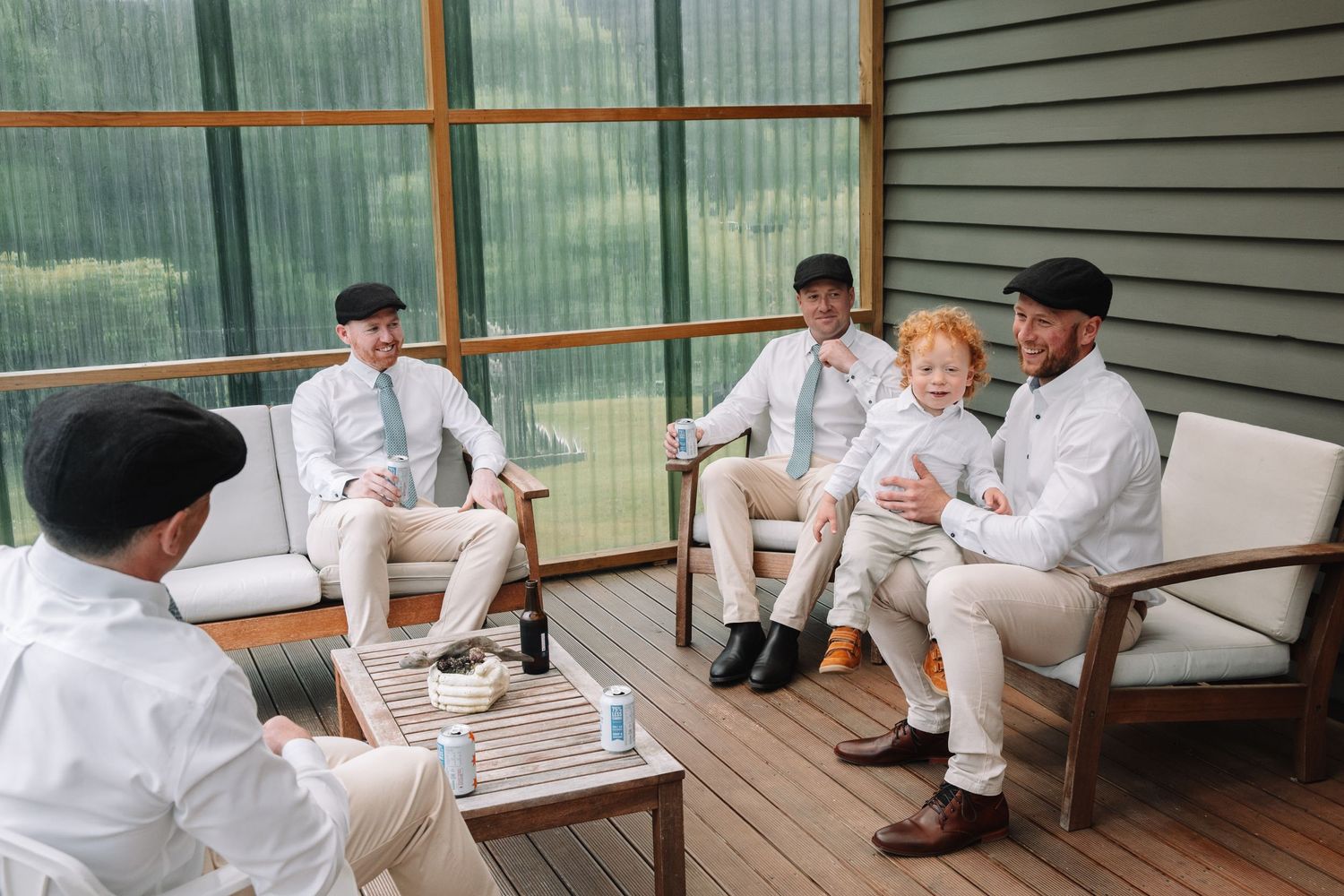 Group gathering in formal attire on a covered deck with glass windows.