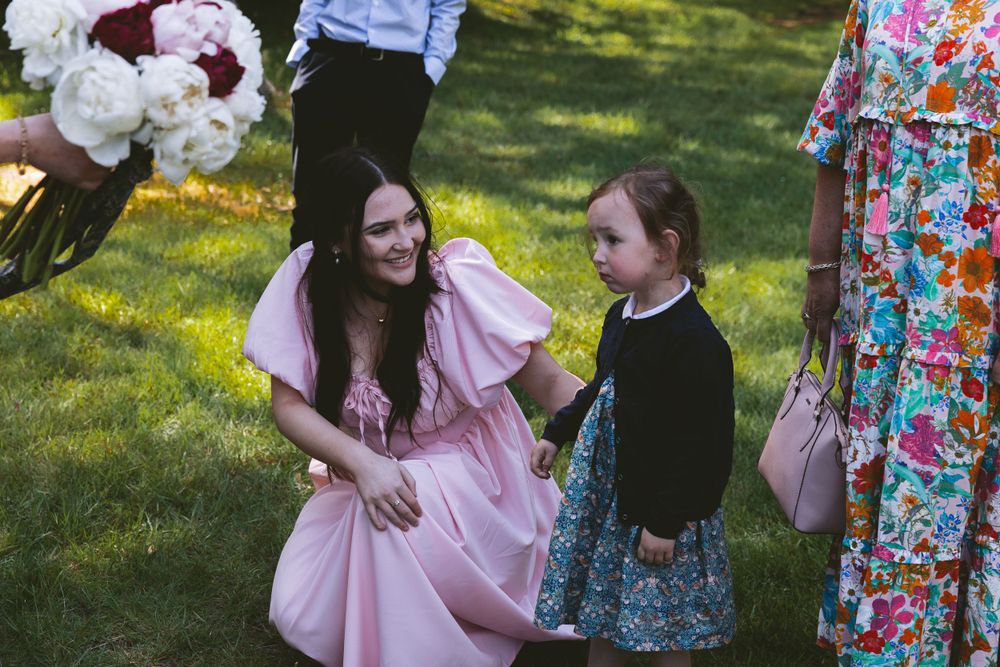 Guests in colorful dresses mingling on a sunlit lawn during an outdoor celebration.