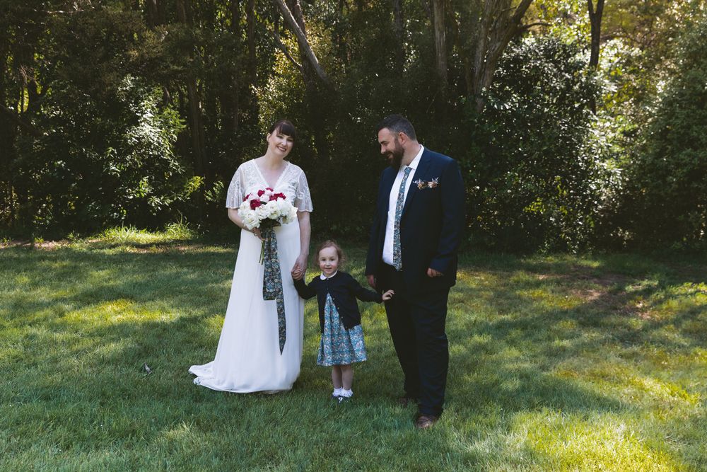 Wedding party standing together on green grass with forest backdrop.
