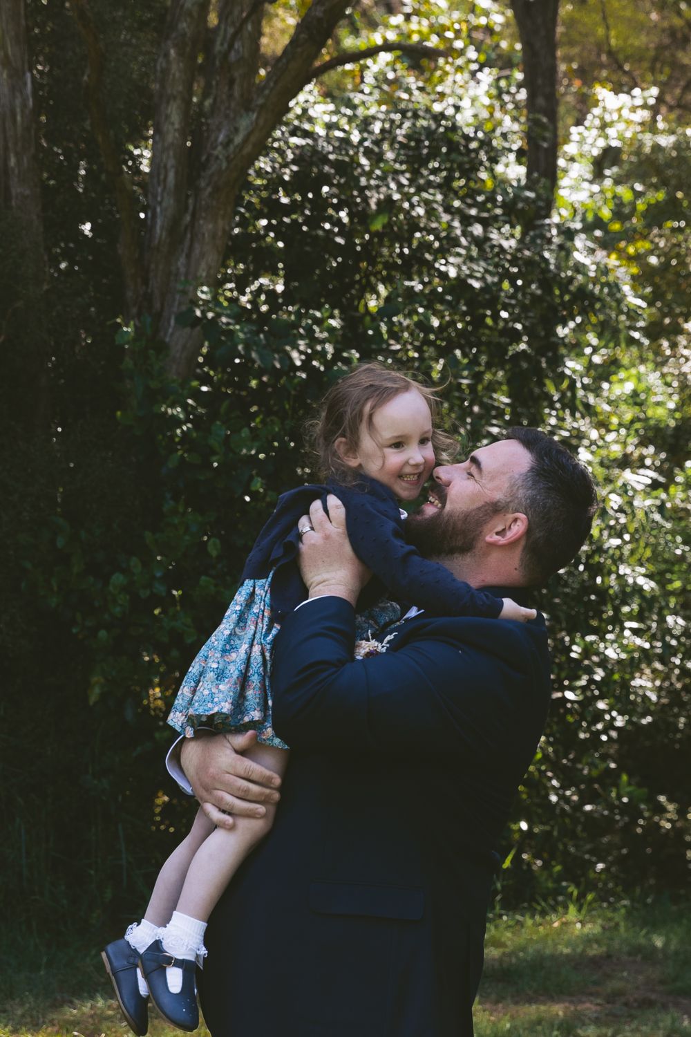 Playful moment between parent and child against sunlit flowering trees.