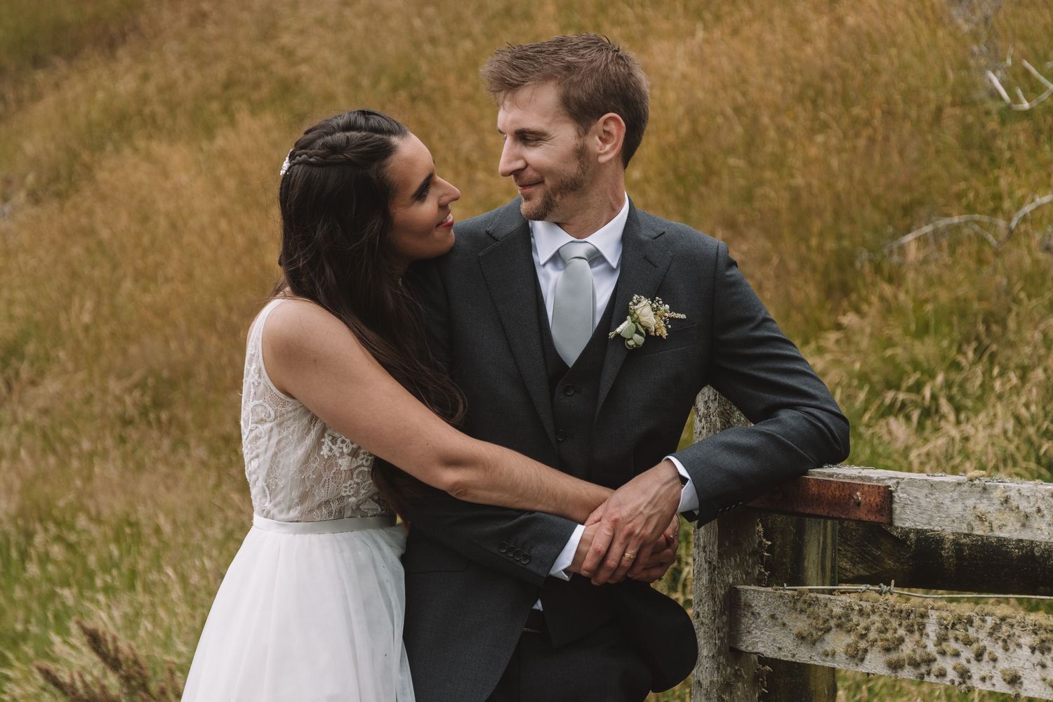 Newlyweds sharing intimate moment against rustic outdoor backdrop.