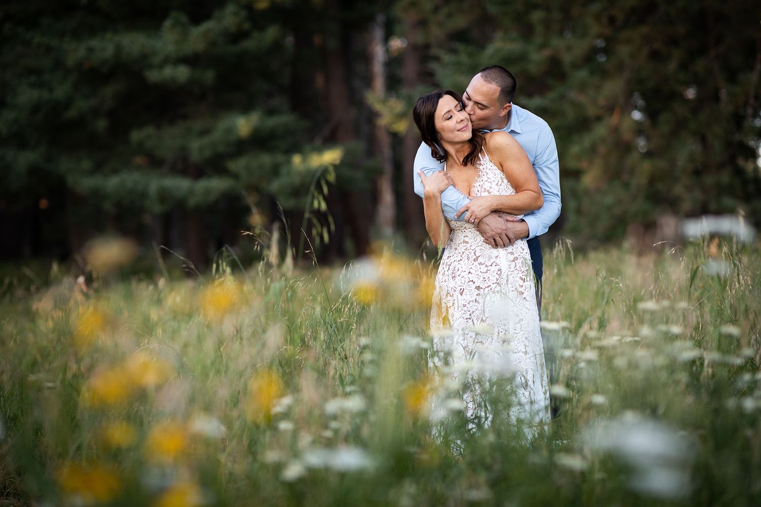 Romantic couple embraces in wildflower meadow during golden hour.