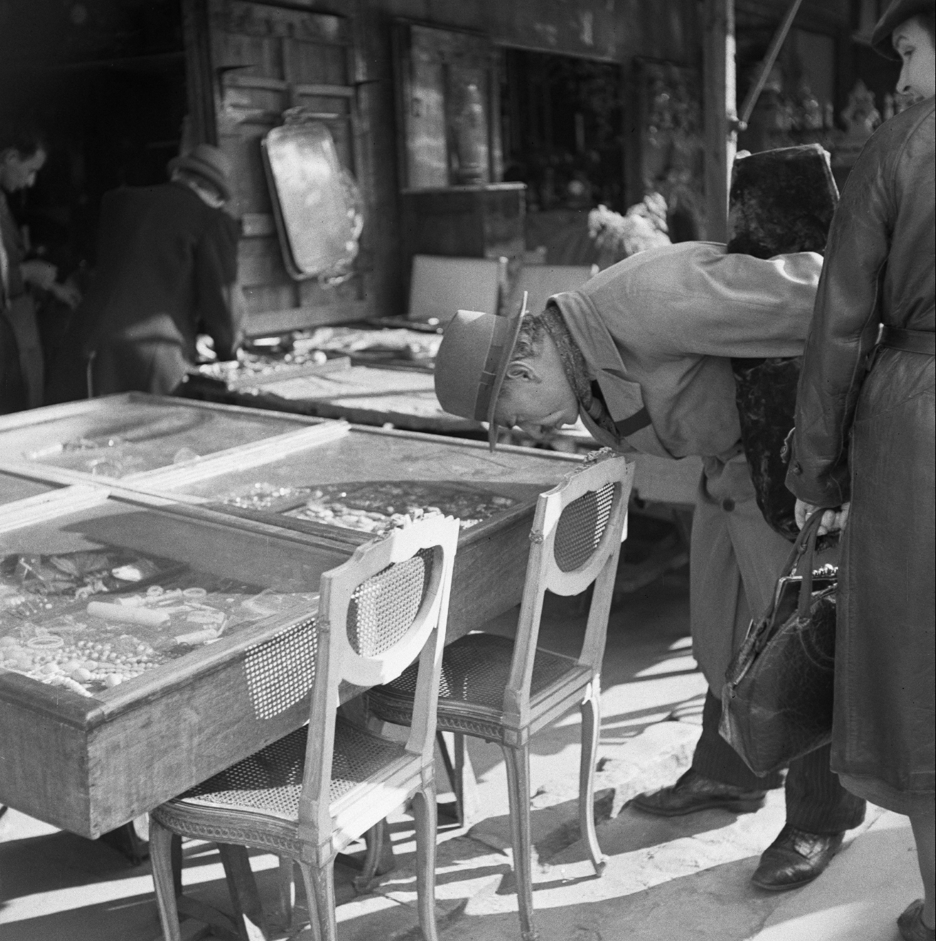 Historical black and white photograph of people browsing items at a market stall.