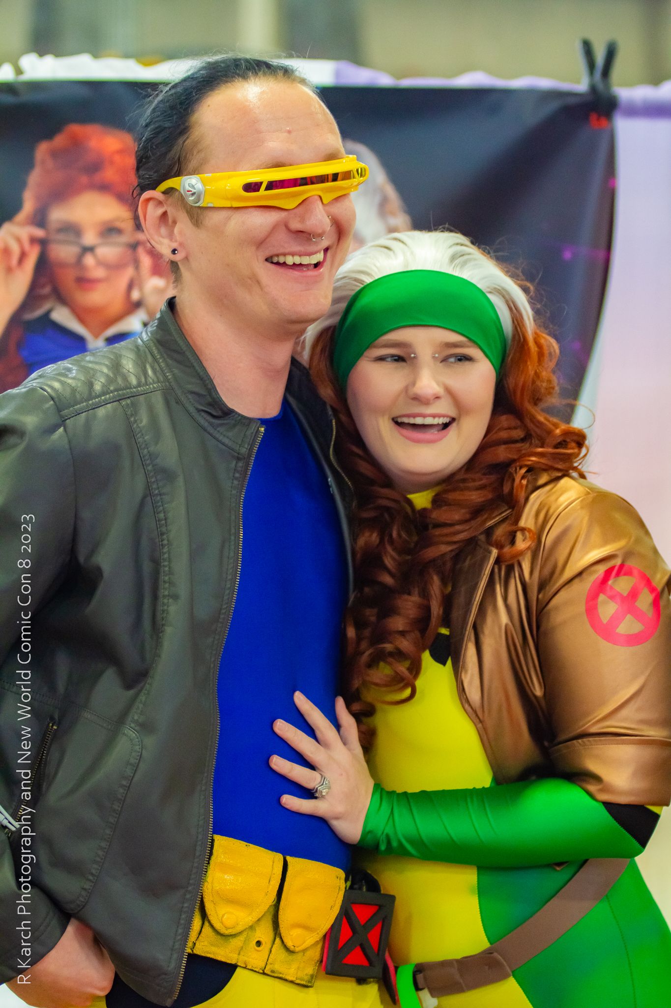 Two X-Men cosplayers pose together wearing colorful superhero outfits and props.