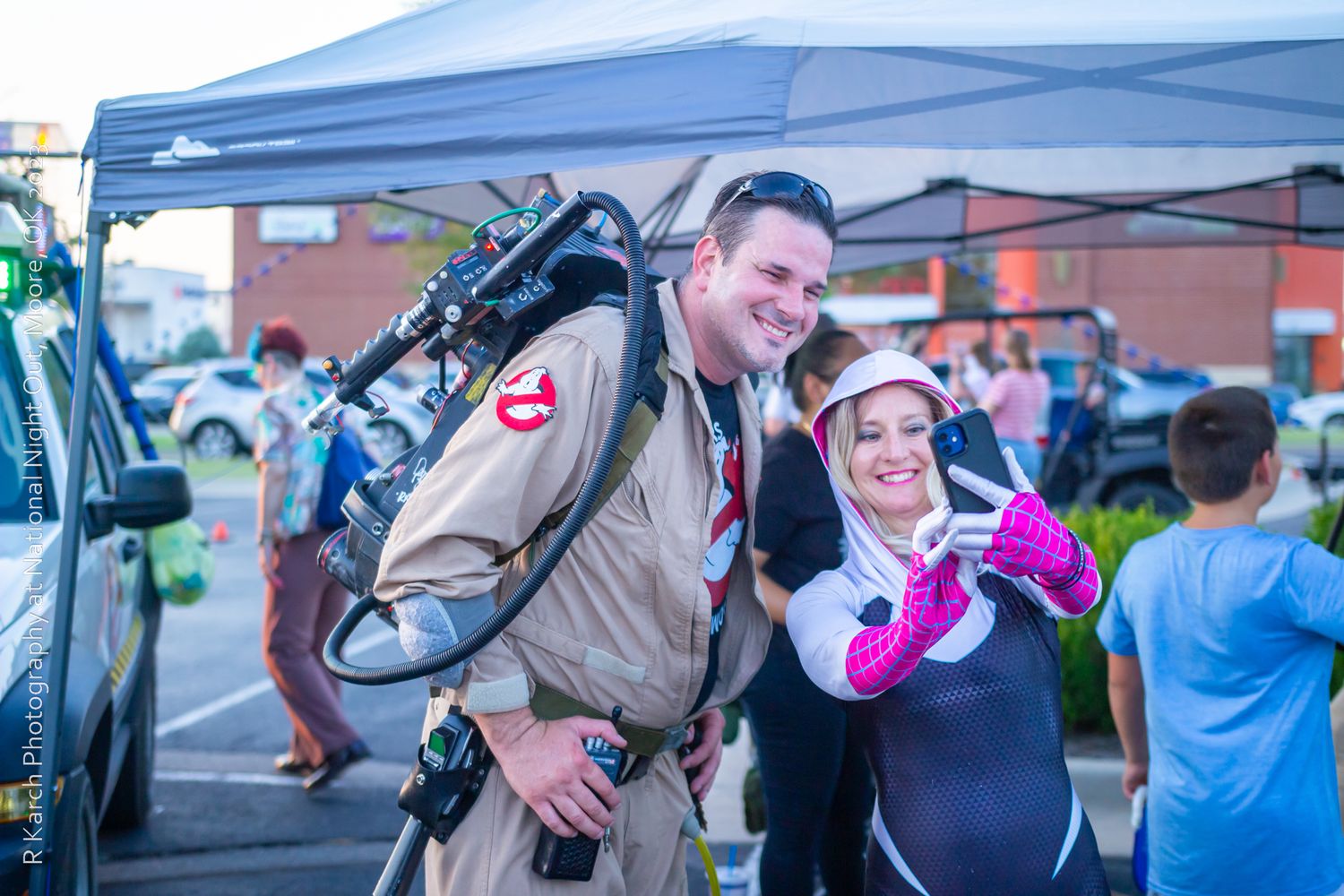 A costumed Ghostbusters fan poses with an attendee at an outdoor convention event.