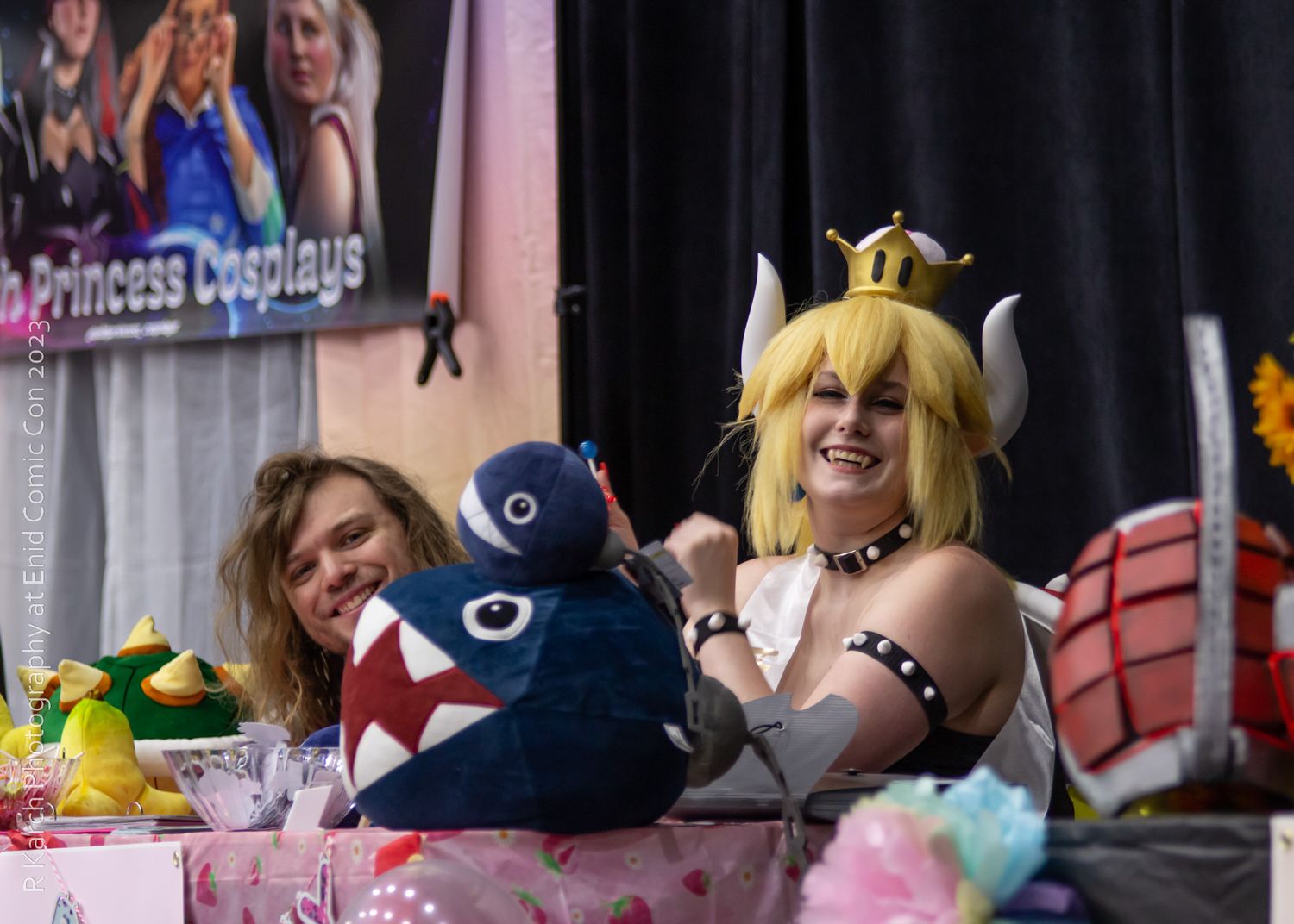 Cosplayers gather around a decorated table with stuffed animals and princess-themed decor.