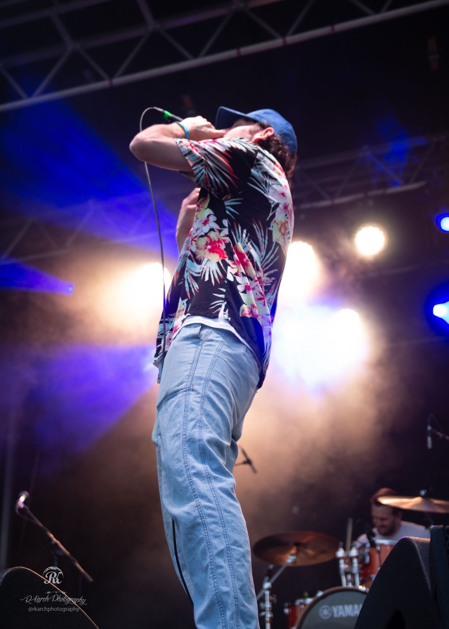 Performer on stage in casual attire singing into microphone with blue stage lighting.