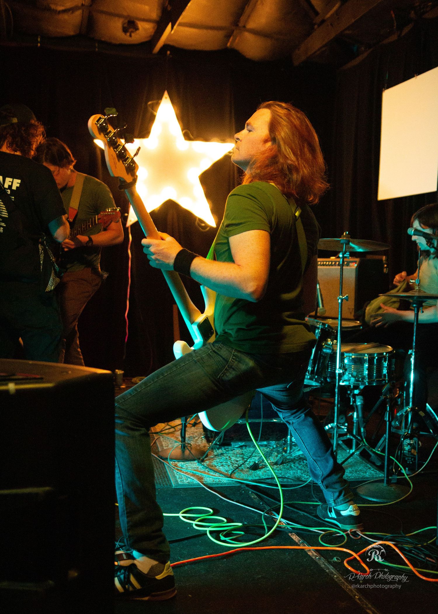 Musician playing guitar on stage with illuminated star decoration in the background.