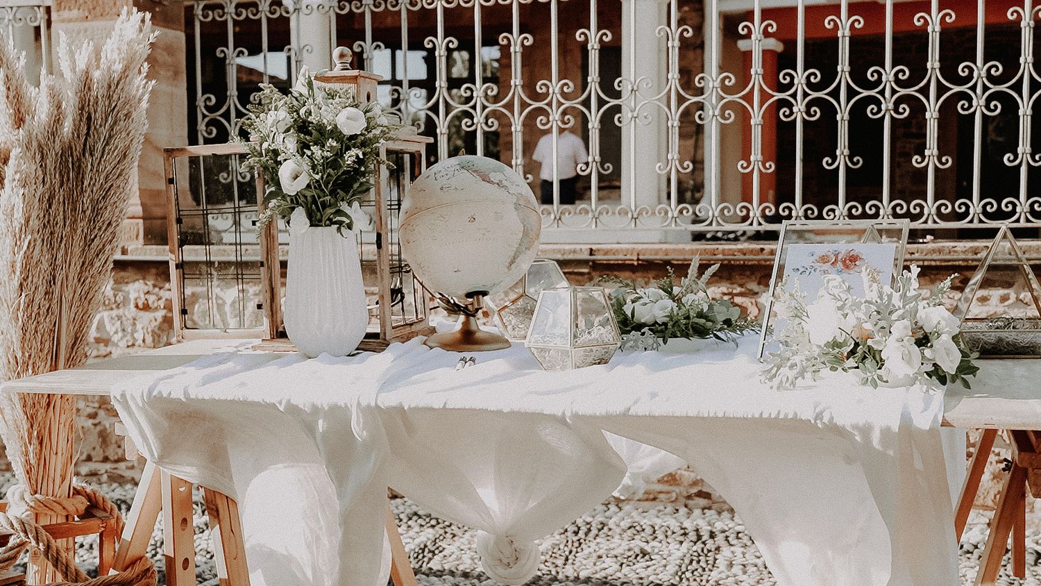 Elegant table setting with vintage decor, globe, and pampas grass against white railing.